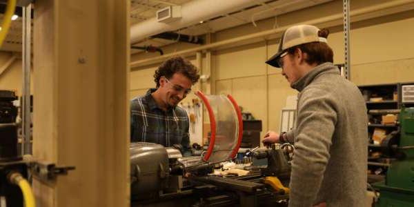 Two students working with machinery wearing safety goggles